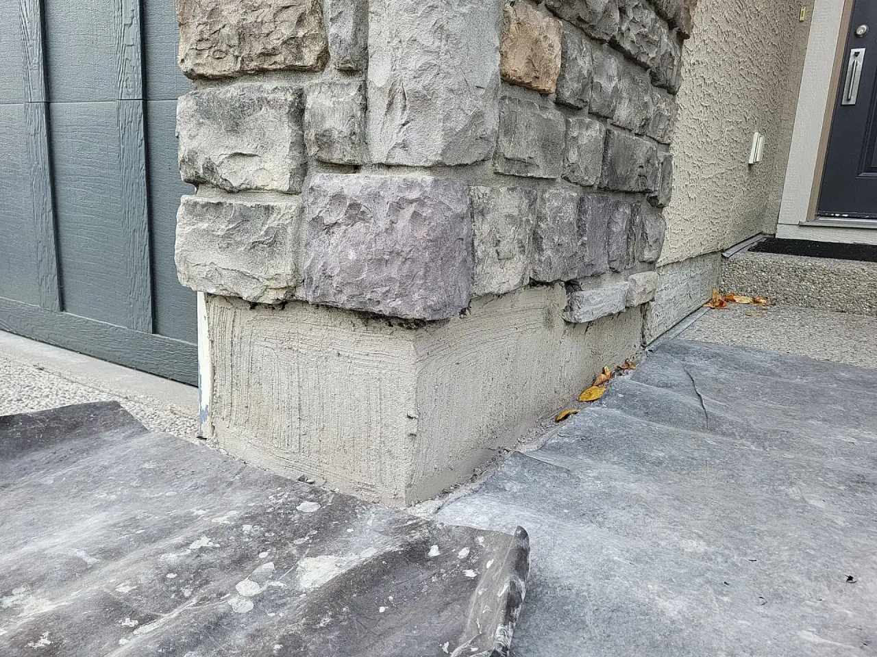 Damaged natural stone at garage wall base in Calgary before repair