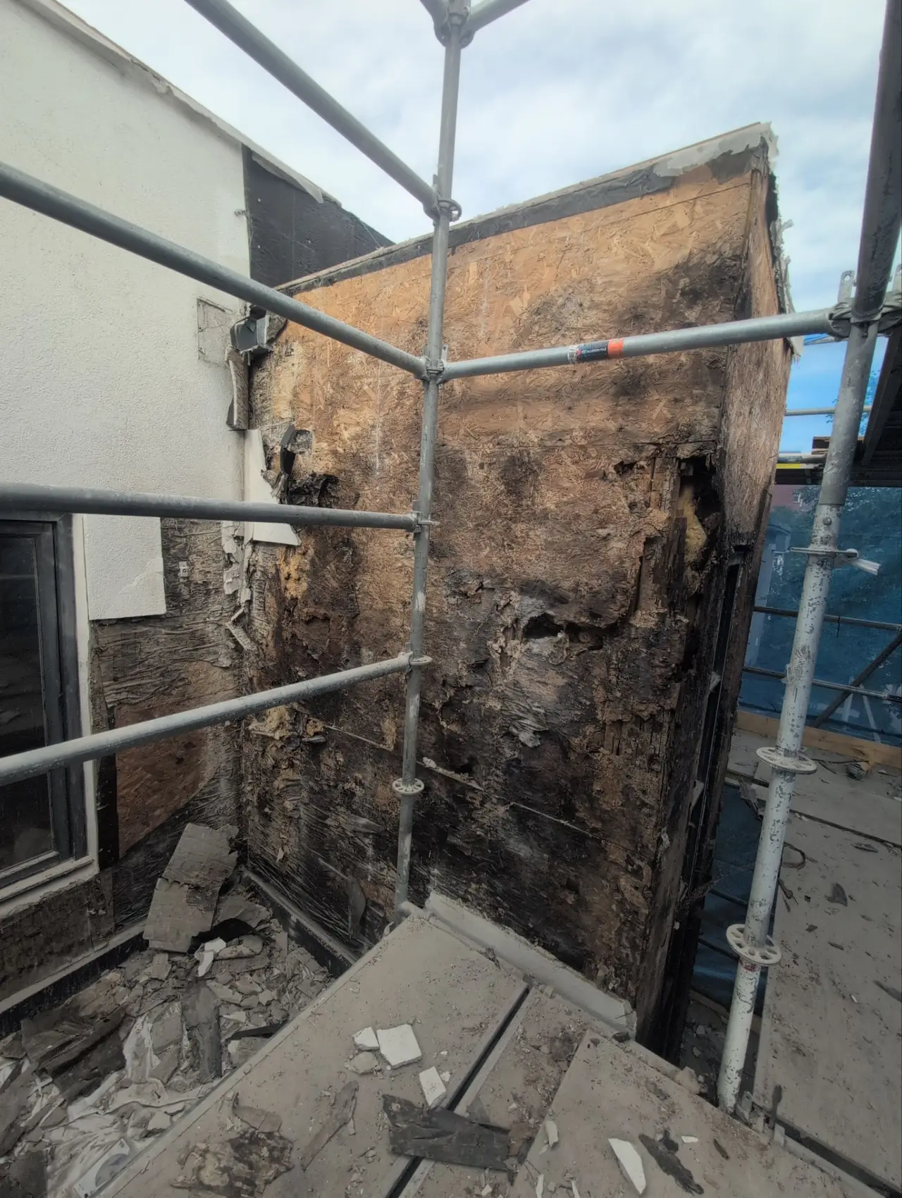 Severely deteriorated OSB wall sheathing, delaminated and blackened by long-term water damage behind stucco