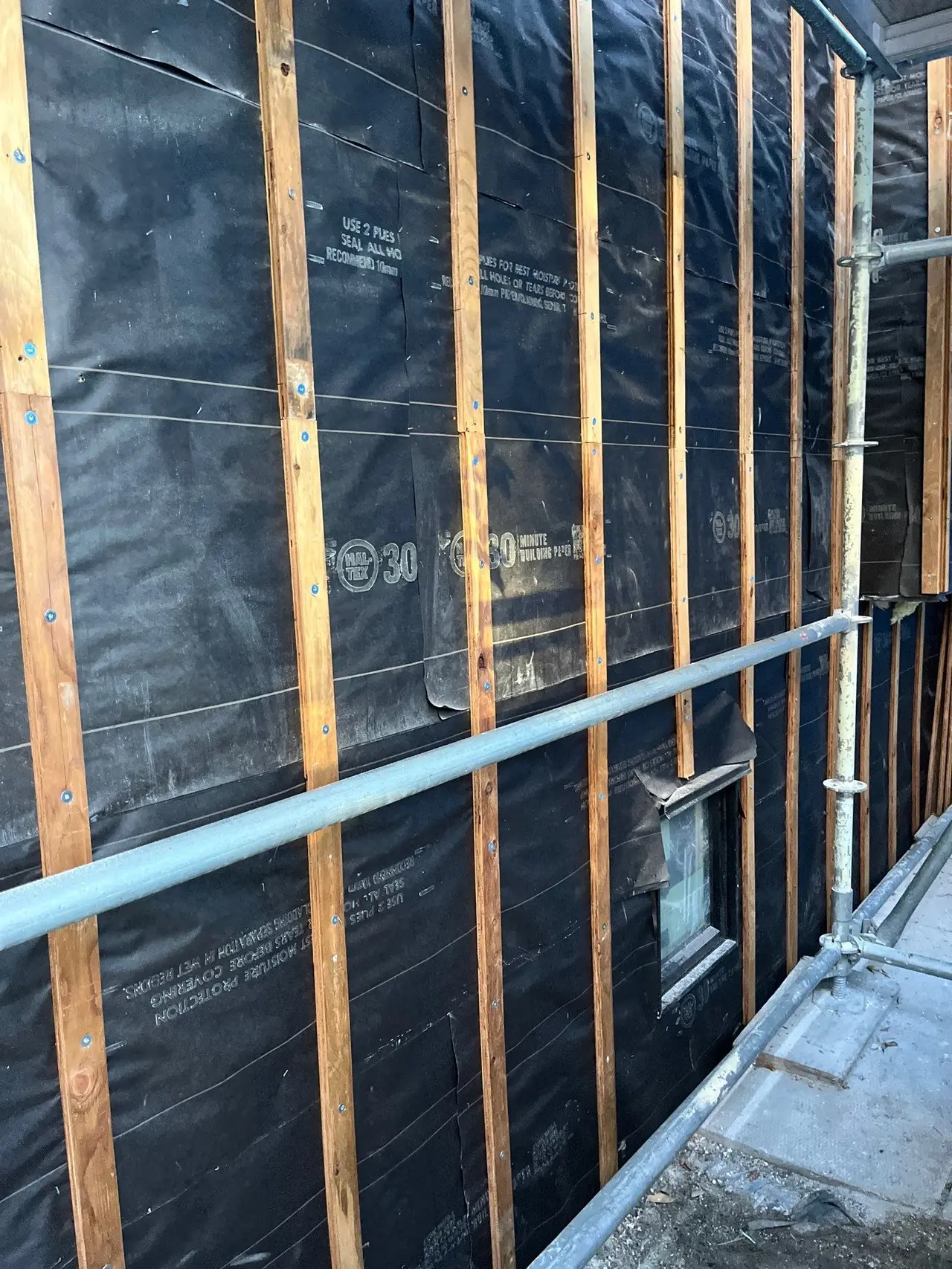 Vertical pressure treated strapping over two layers of building paper, forming the rainscreen cavity behind stucco