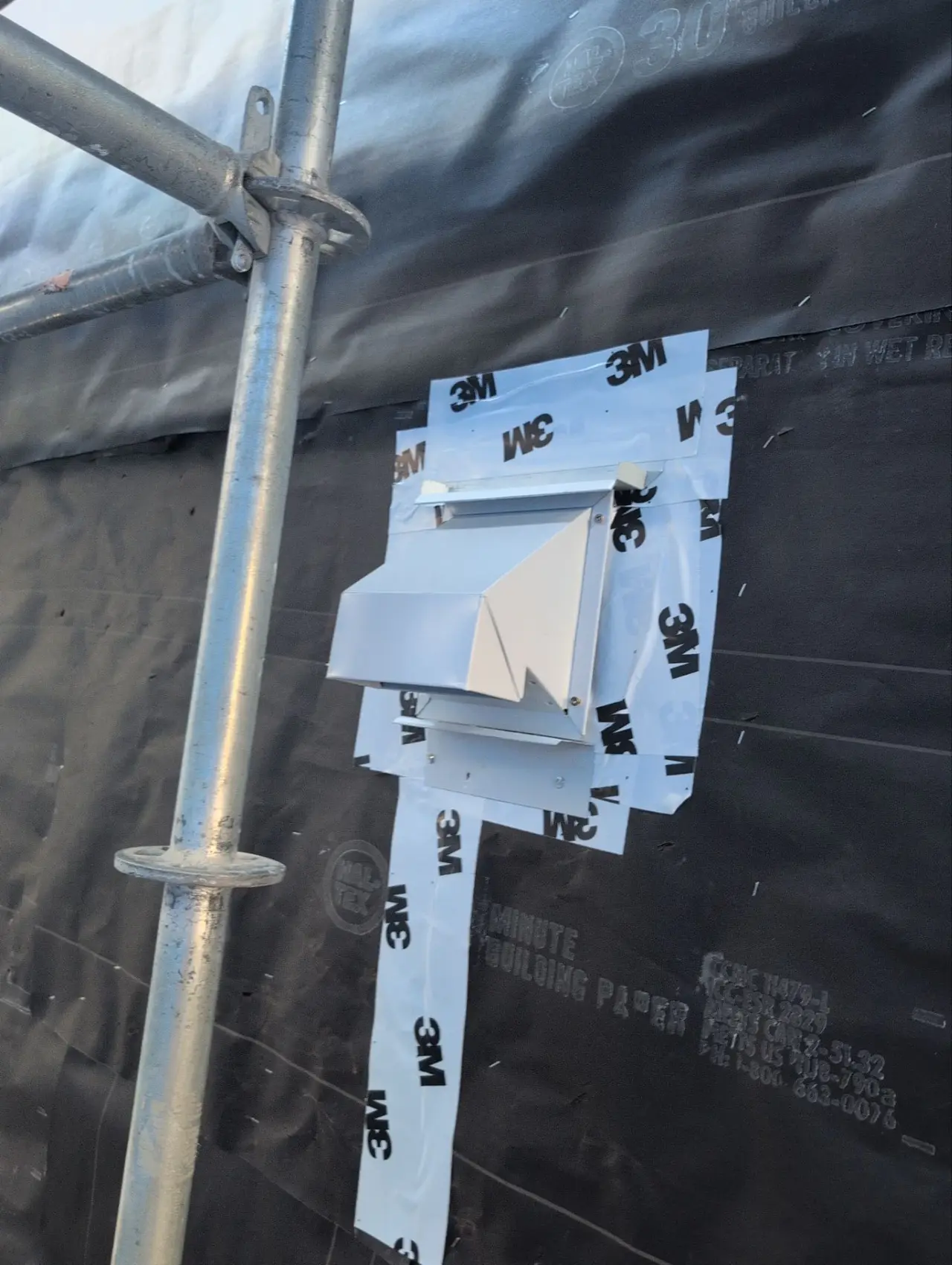 Head flashing with folded end dams and a self-adhered membrane collar installed around a metal hood vent over building paper