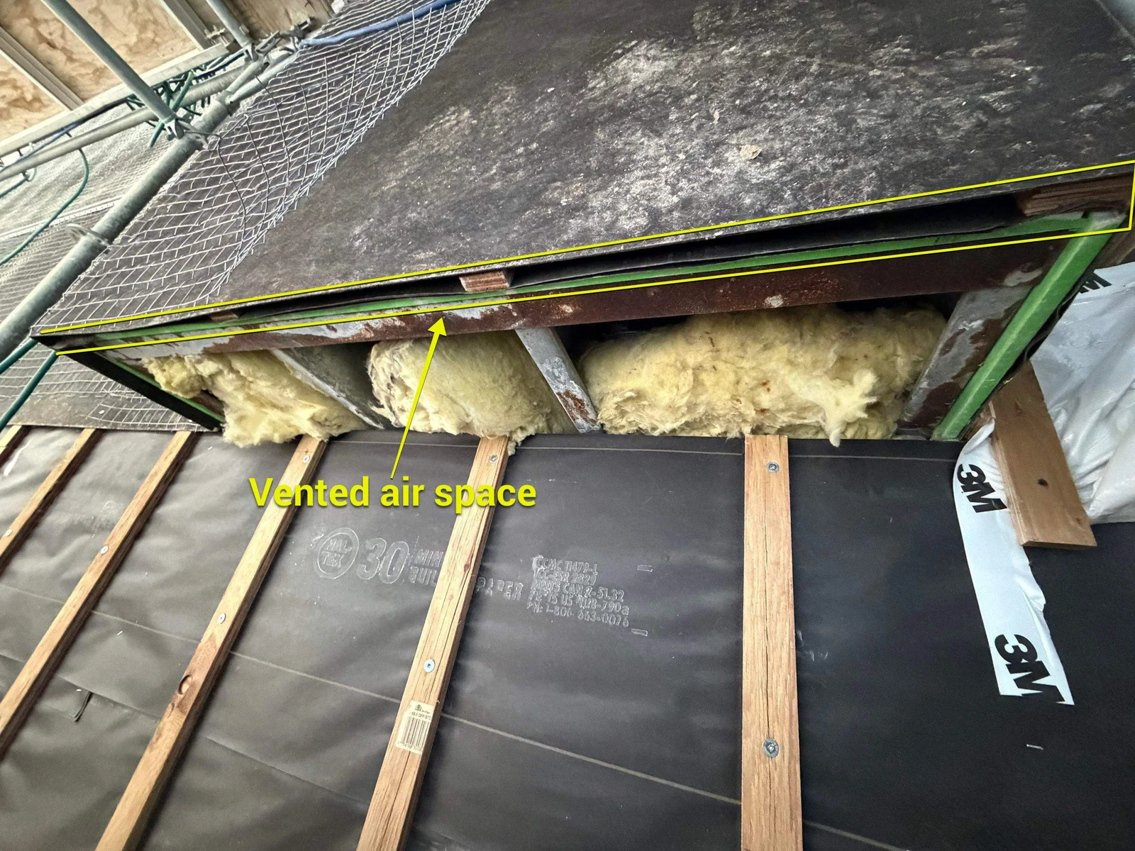 Annotated photo of a rainscreen wall showing the vented air space gap between the stucco cover board and the flashing below, with 30 minute building paper and pressure treated strapping visible on the wall