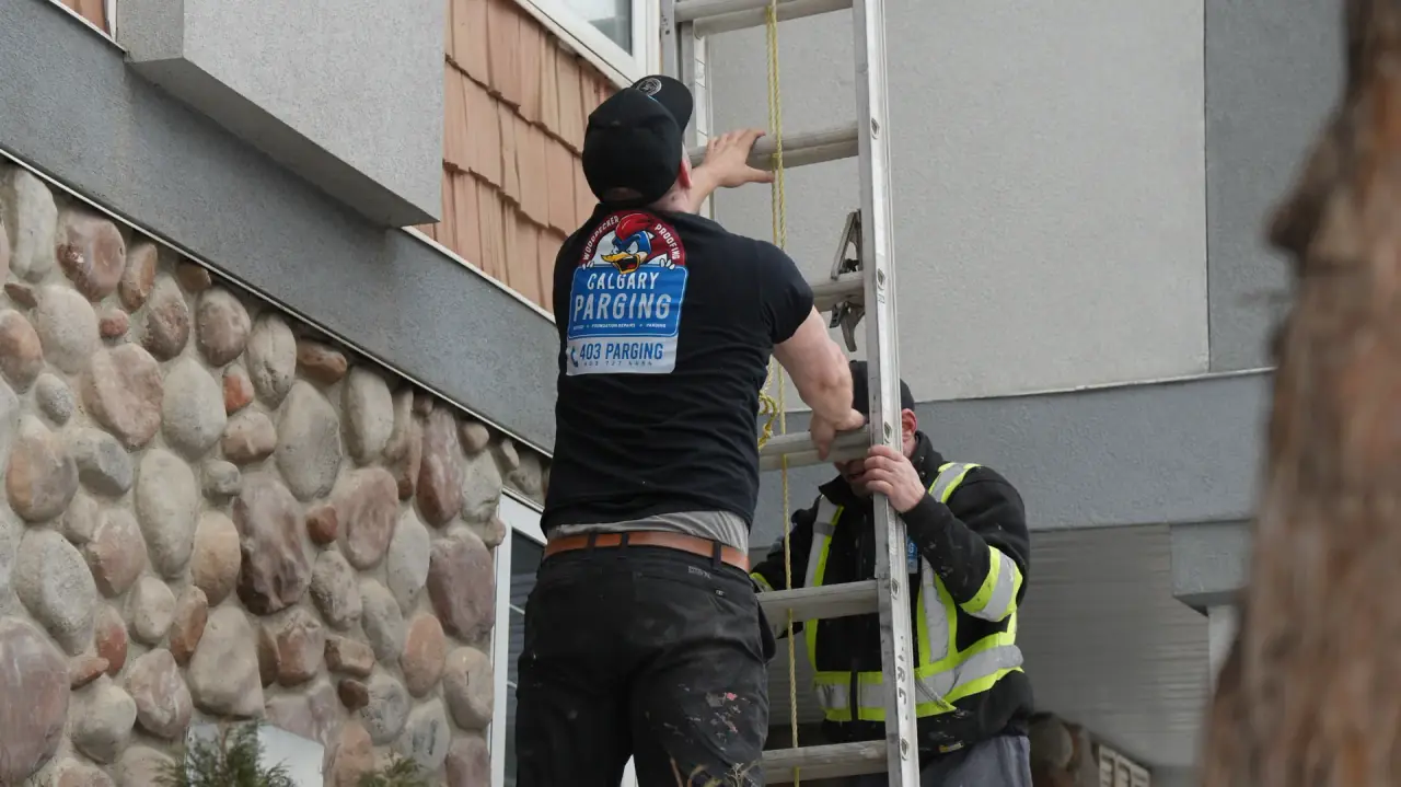 Two Calgary Parging team members setting up a ladder to reach and repair woodpecker-damaged stucco